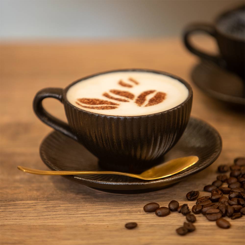 Cappuccino with latte art in a Black textured cup and saucer on a wooden table with coffee beans.