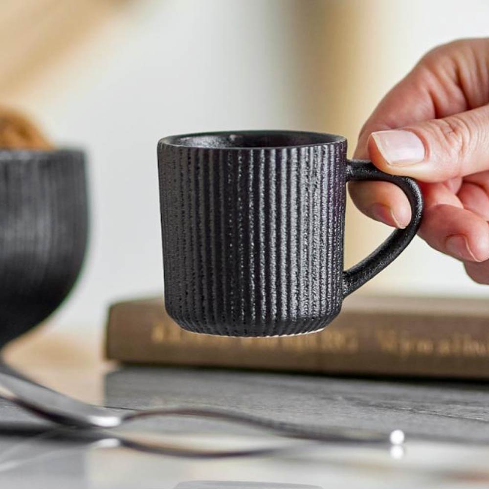 Neri Stoneware Espresso Cup in Black held in hand above kitchen table
