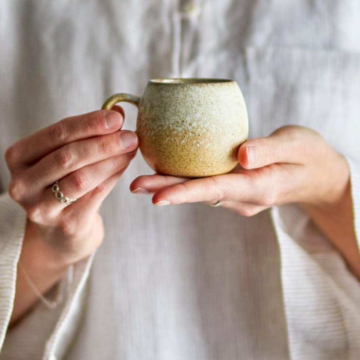 Paula Stoneware Espresso Cup in natural golden glaze, featuring a small round design and a comfortable handle, held in hand for a cosy coffee moment.