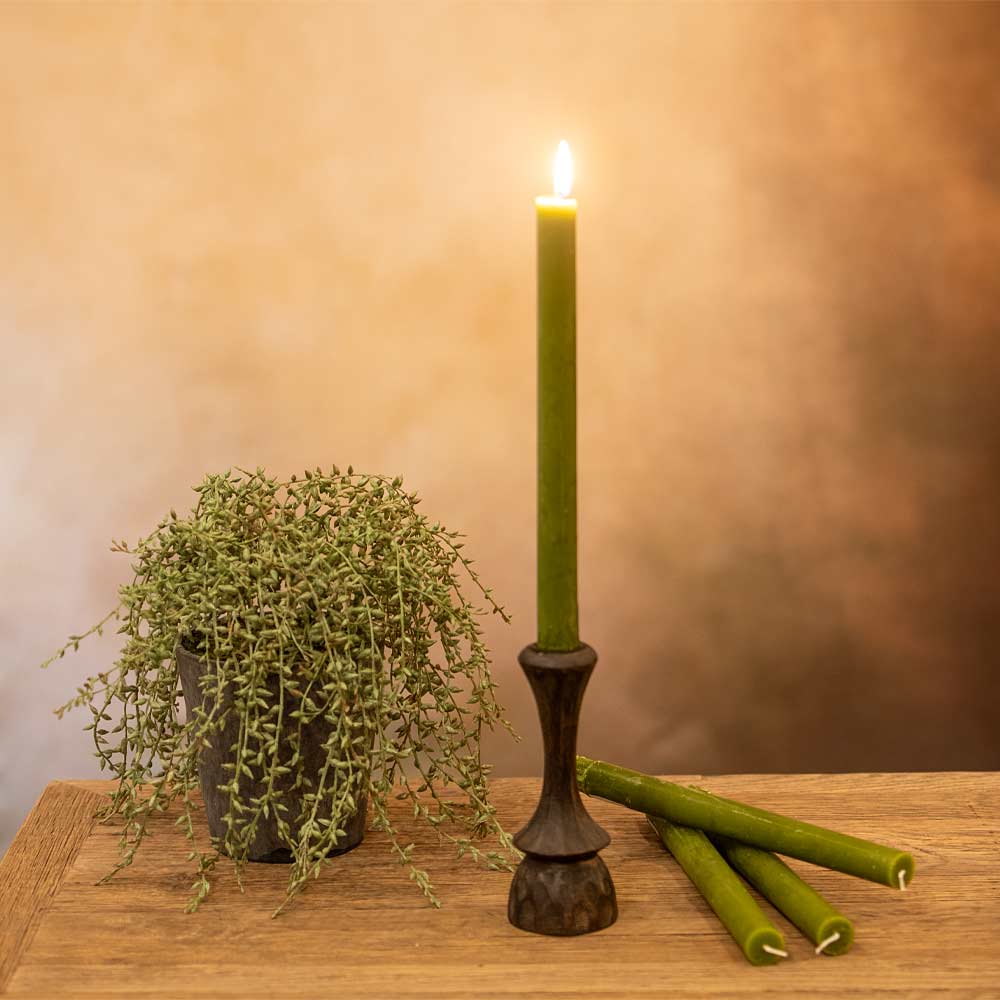 Fern green rustic dinner candle on a wooden console with a warm diffused background