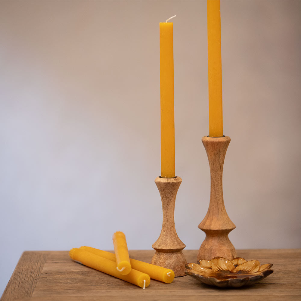 Two wooden candlesticks with ochre  candles on a wooden surface.