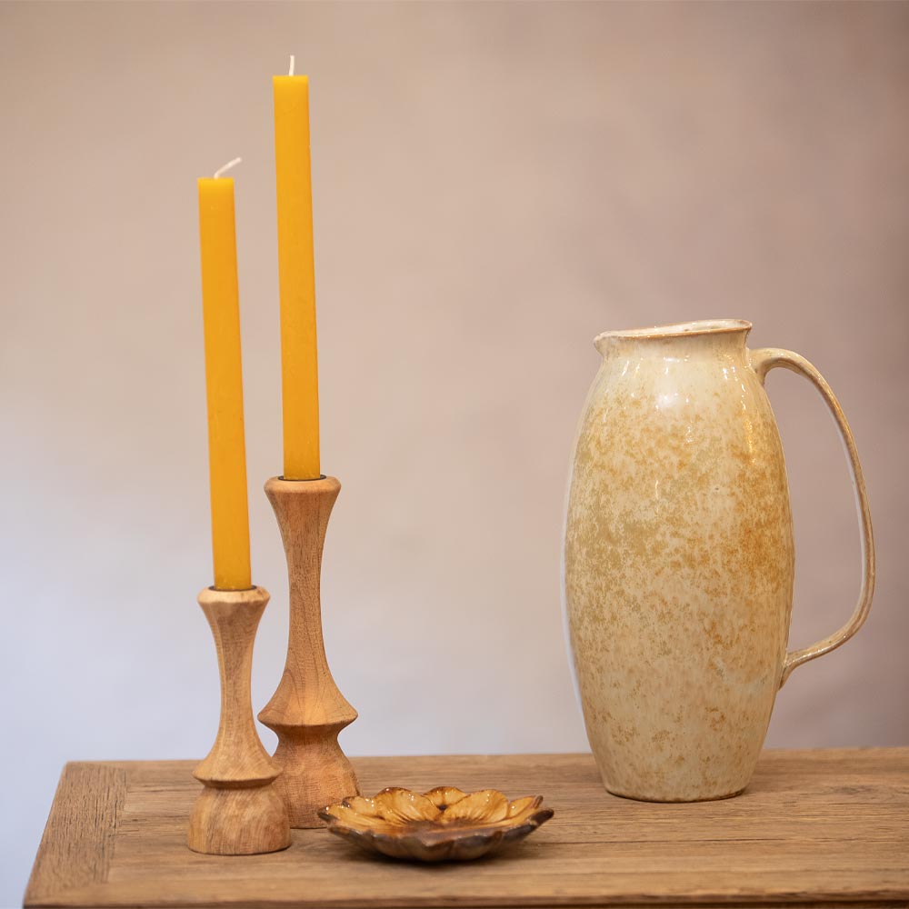 Ceramic pitcher, wooden candle holders with candles, and a small dish on a wooden surface.