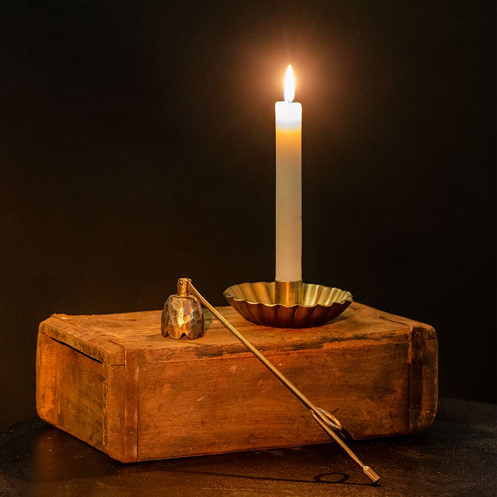 White Candle in a Scalloped brass holder on a wooden brick mould with a dark background