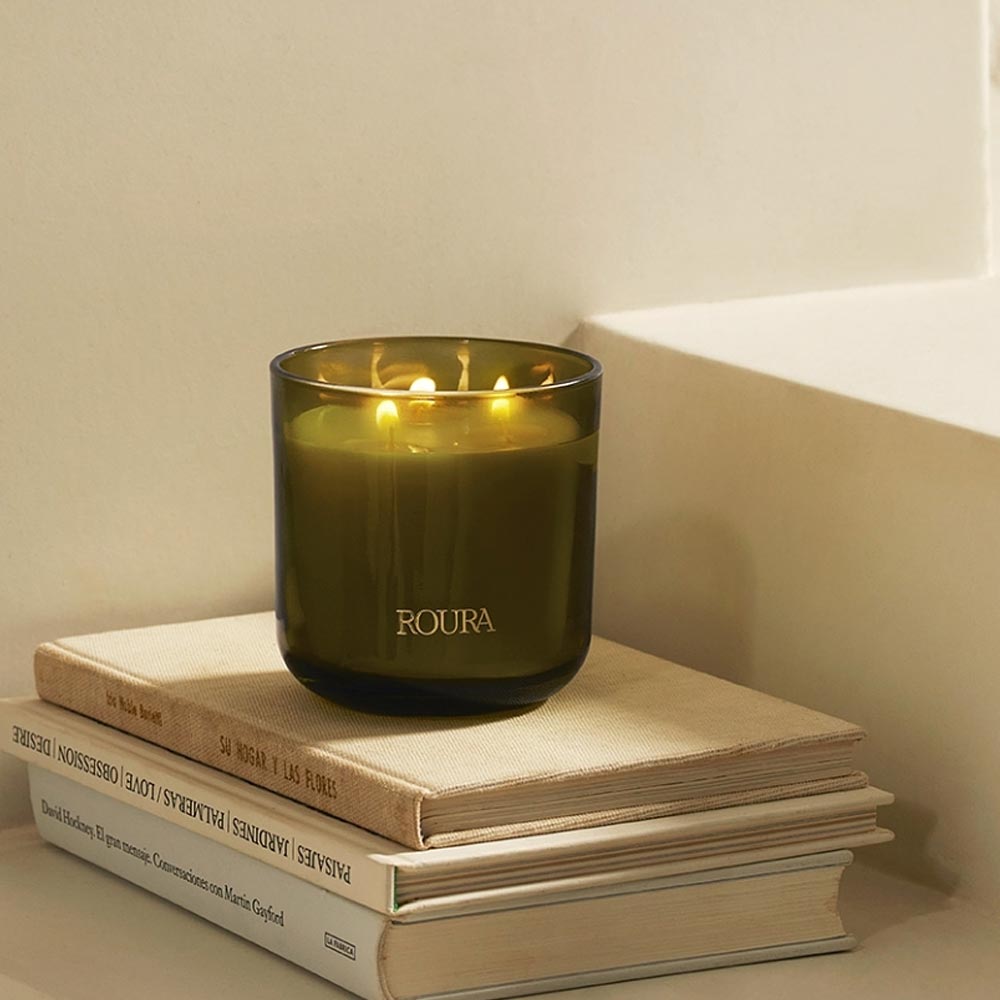 Secret Garden 3 Wick Green Candle by Roura on a stack of books against a neutral background