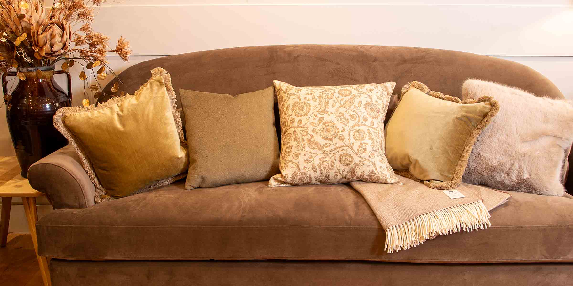 Brown sofa with patterned cushions and a blanket in a cosy living room setting.