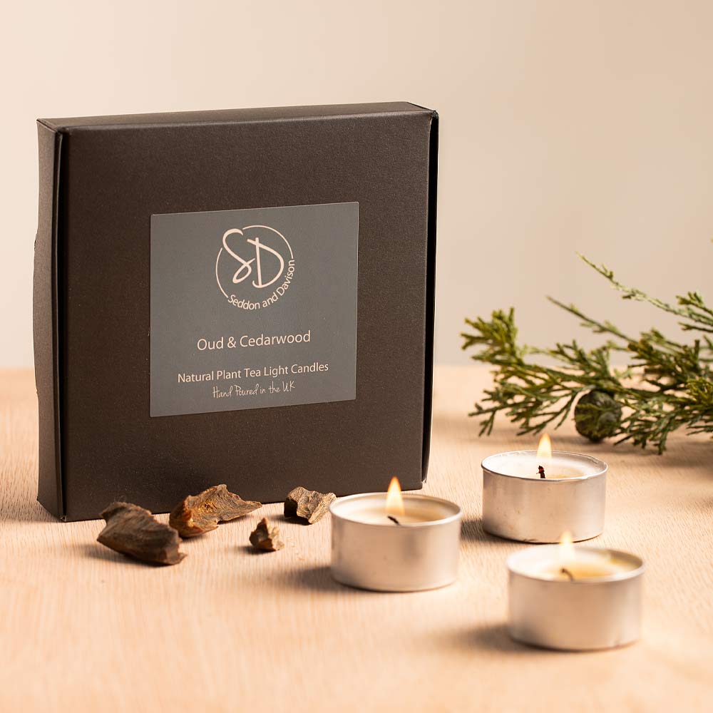 Oud & Cedarwood Tea Lights with packaging and natural elements on a beige surface