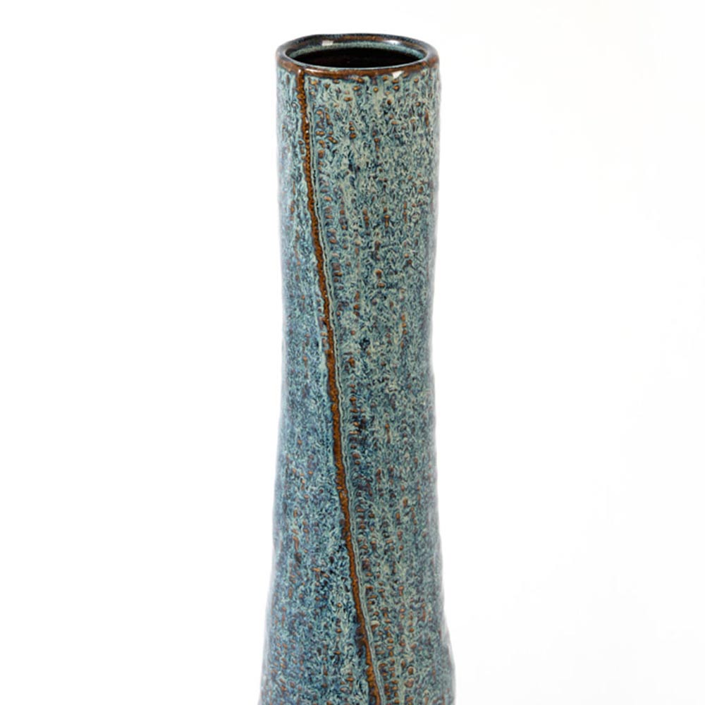 A close-up of a tall, slender ceramic vase with a textured blue and brown glaze, a vertical brown raised overlap forming a ridge in the central area is also shown as it sits against a plain white background.