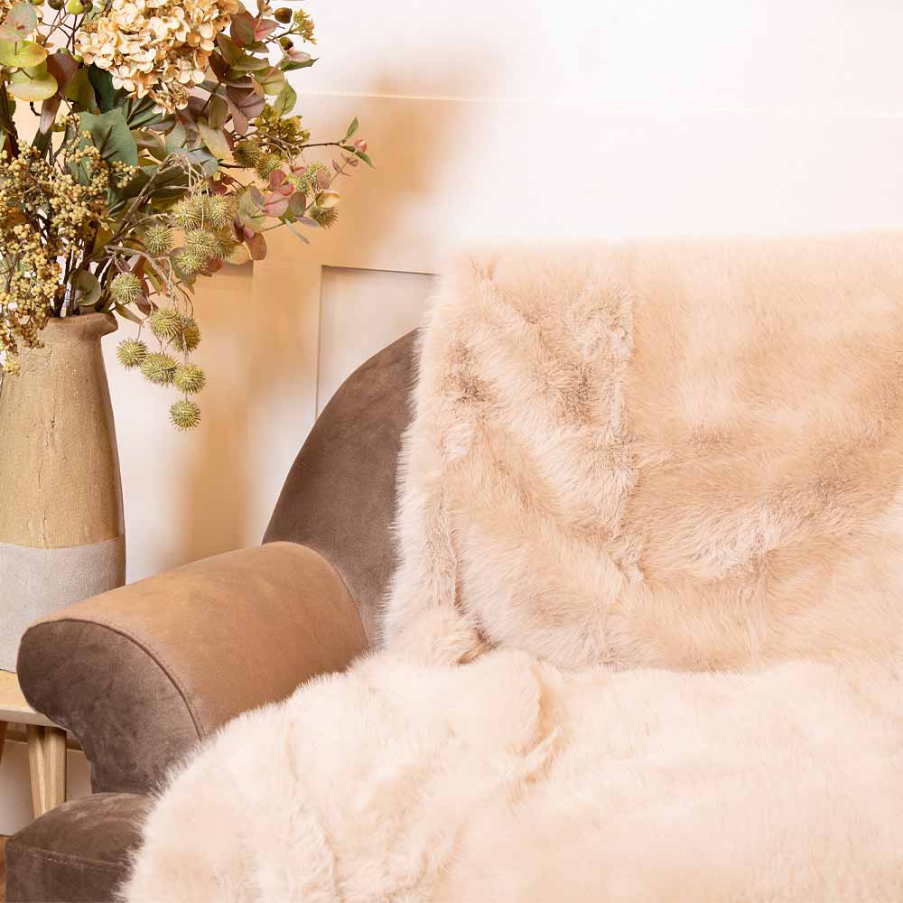 Close-up of a fluffy Sloane Mink Faux Fur Throw draped over a chair with a vase of flowers in the background.