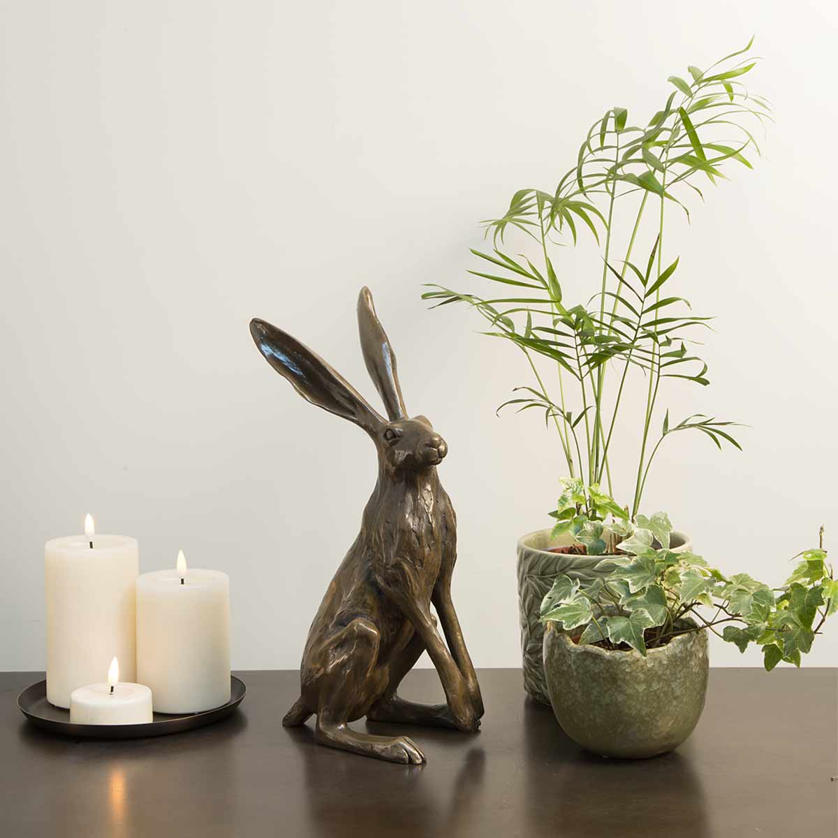 Startled Hare sculpture in bronze resin – handmade in the UK from original artwork by Joanna Martins - Displayed with candles and plants