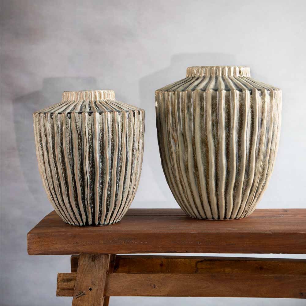 Two ribbed decorative vases with a distressed olive and beige finish, displayed on a rustic wooden bench against a textured gray wall.