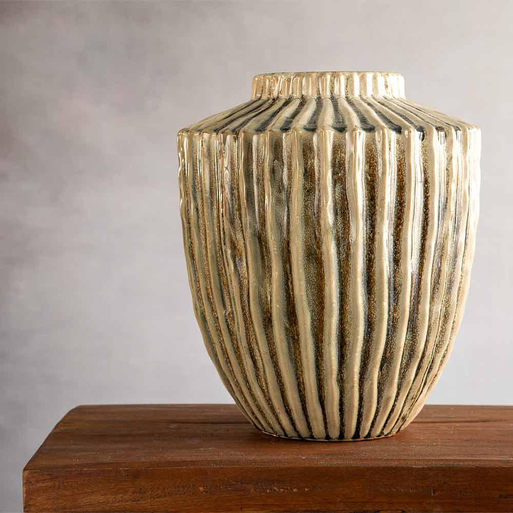 A ribbed ceramic vase with a textured Olive and beige finish, displayed on a wooden surface against a neutral gray background.
