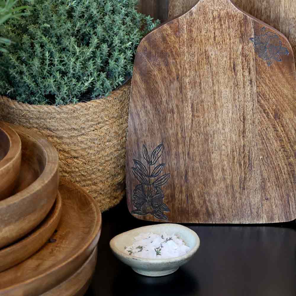 Tours Wooden Tapas Board with Flower Carving next to stacked wooden bowls and a small bowl of salt on a dark surface.