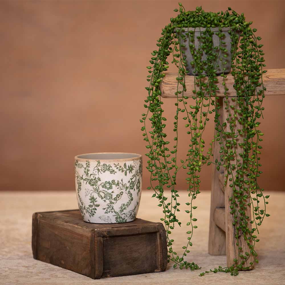 One faux potted plants on a wooden surface with two floral pots near by against a brown background 