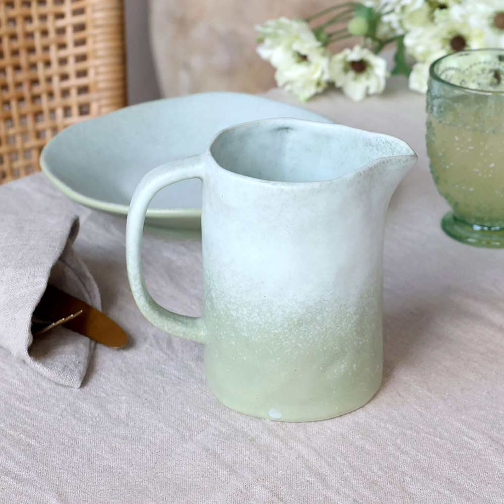Light green Valence Porcelain Jug - pitcher and glass on a textured surface with flowers in the background