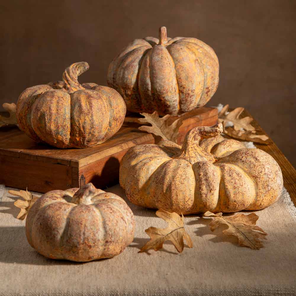 an autumnal scene of Rust coloured stone  pumpkins placed on a beige table runner styled with oak leaves