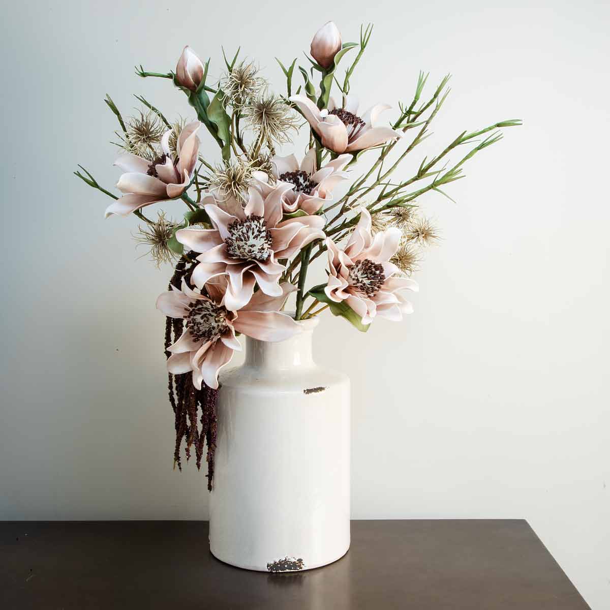 Ivory distressed bottle vase with faux flowers on a dark wood console