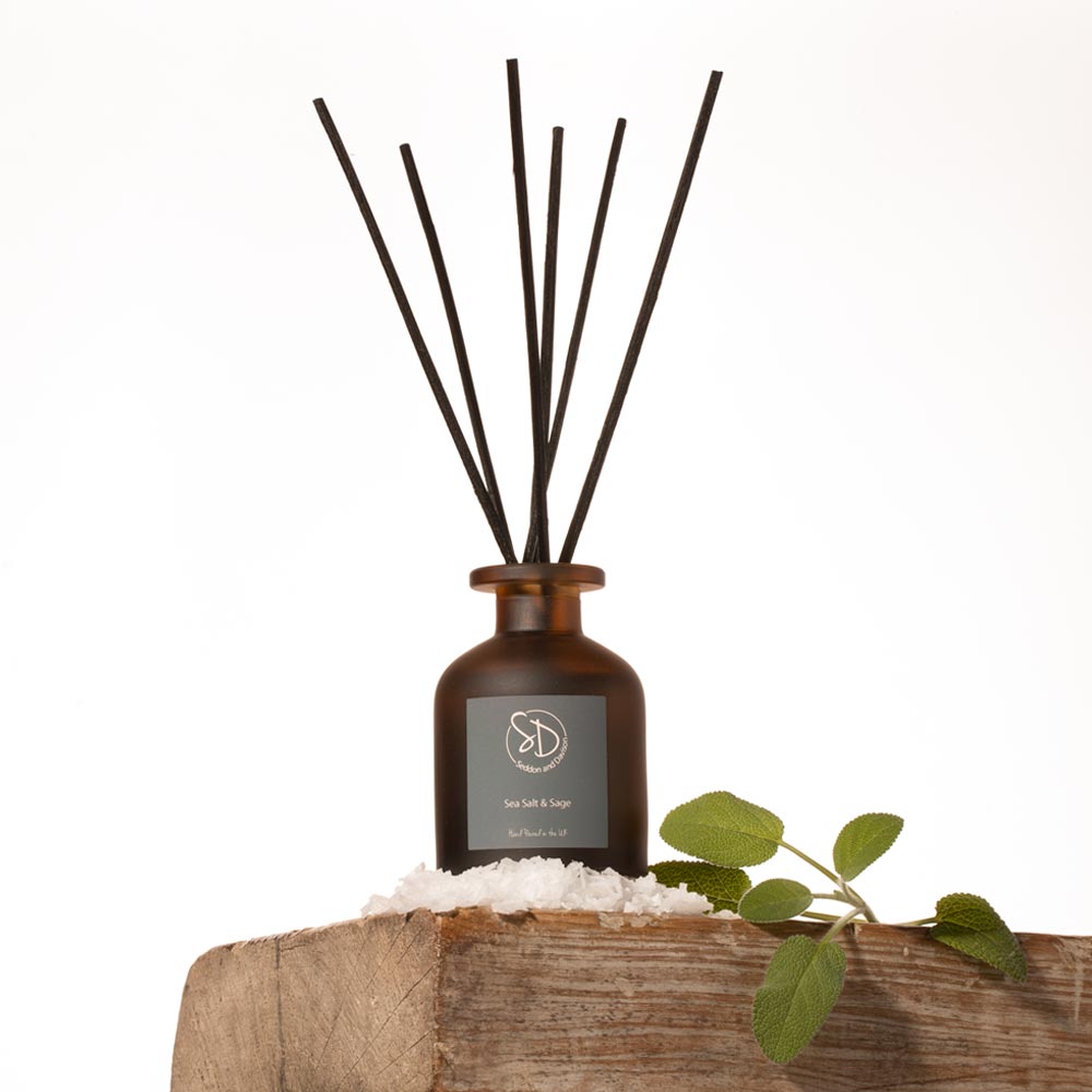 Sea Salt and Sage Reed diffuser with black sticks on a wooden block with a white background